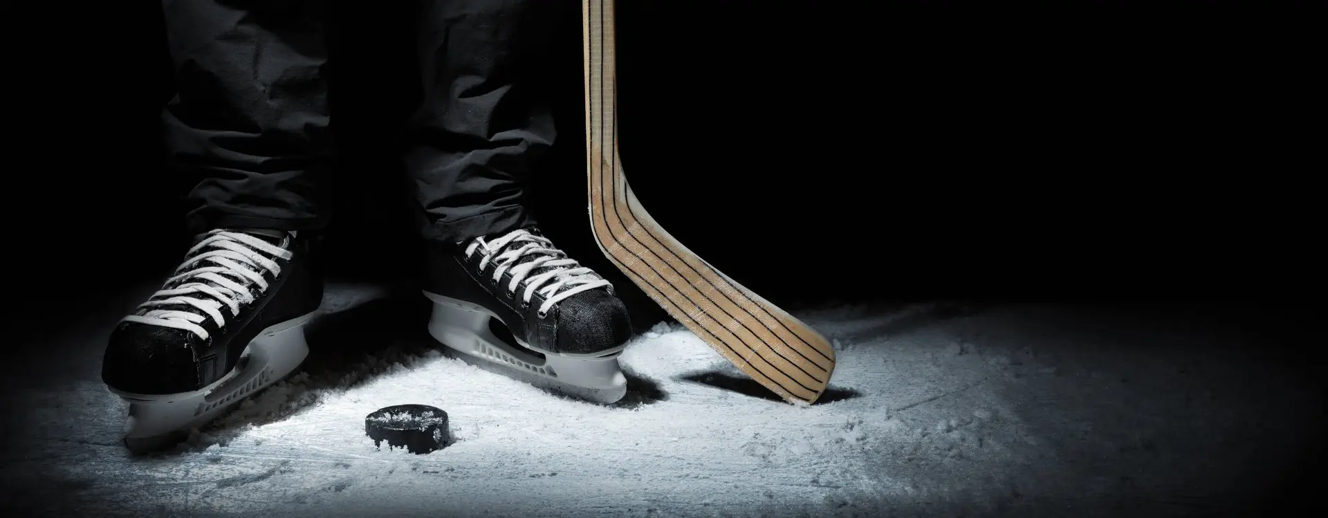 black hockey skates next to a puck and stick on ice rink
