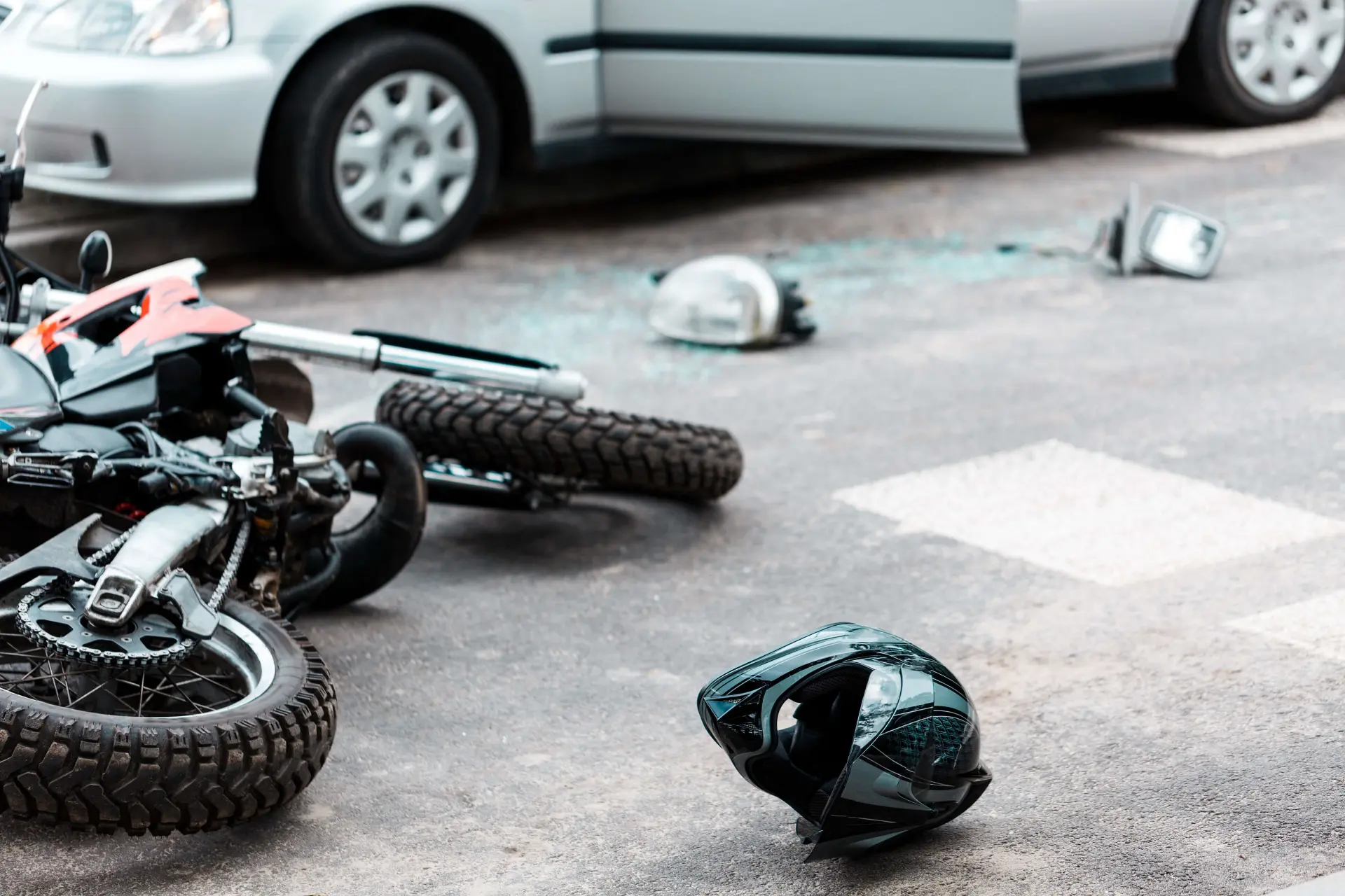 a motorcycle helmet and broken car parts are strewn across a street in the aftermath of a motorcycle colliding with a car