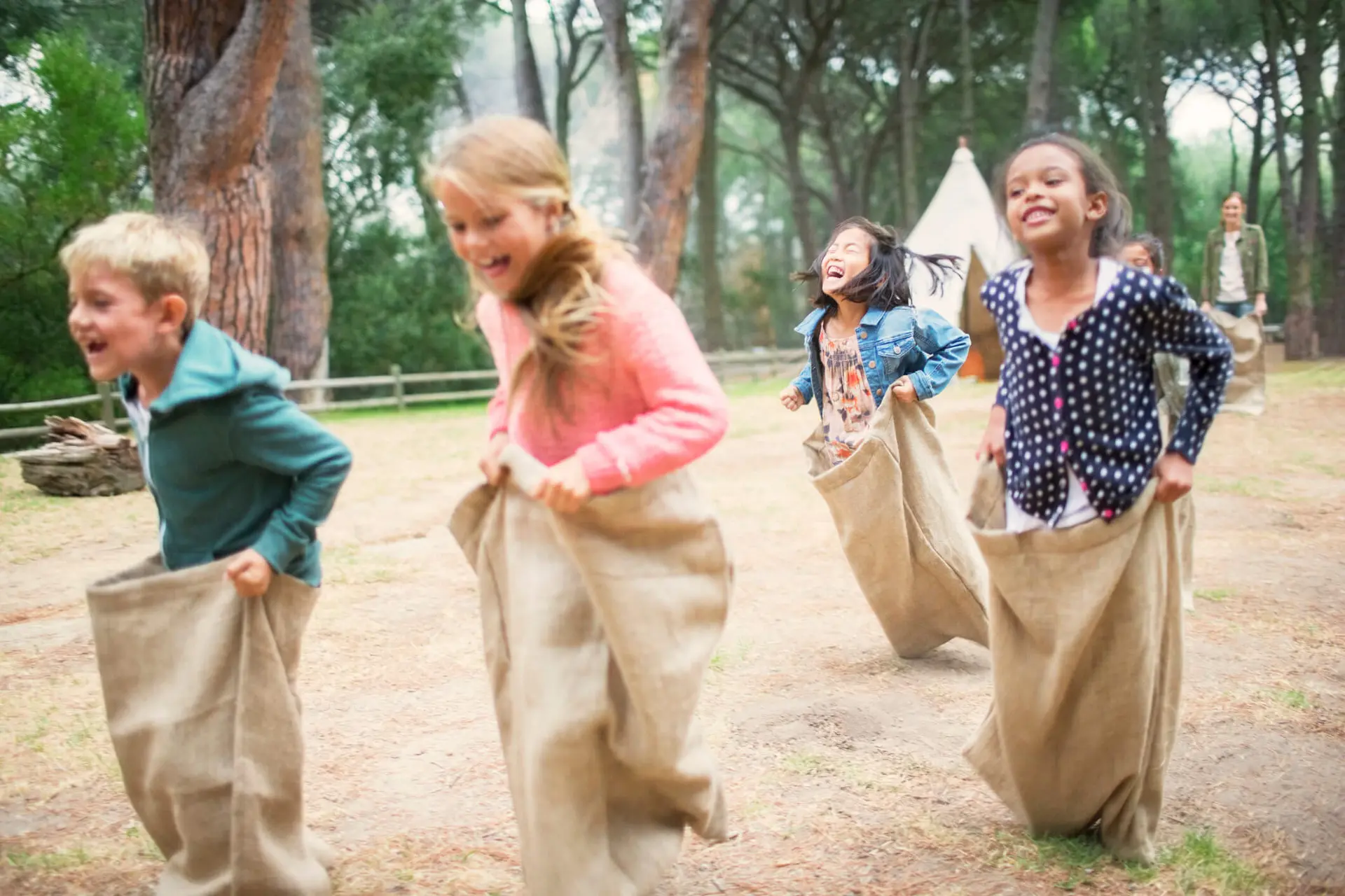 Four children in potato sacks racing. The children are laughing while they are jumping in the sacks.