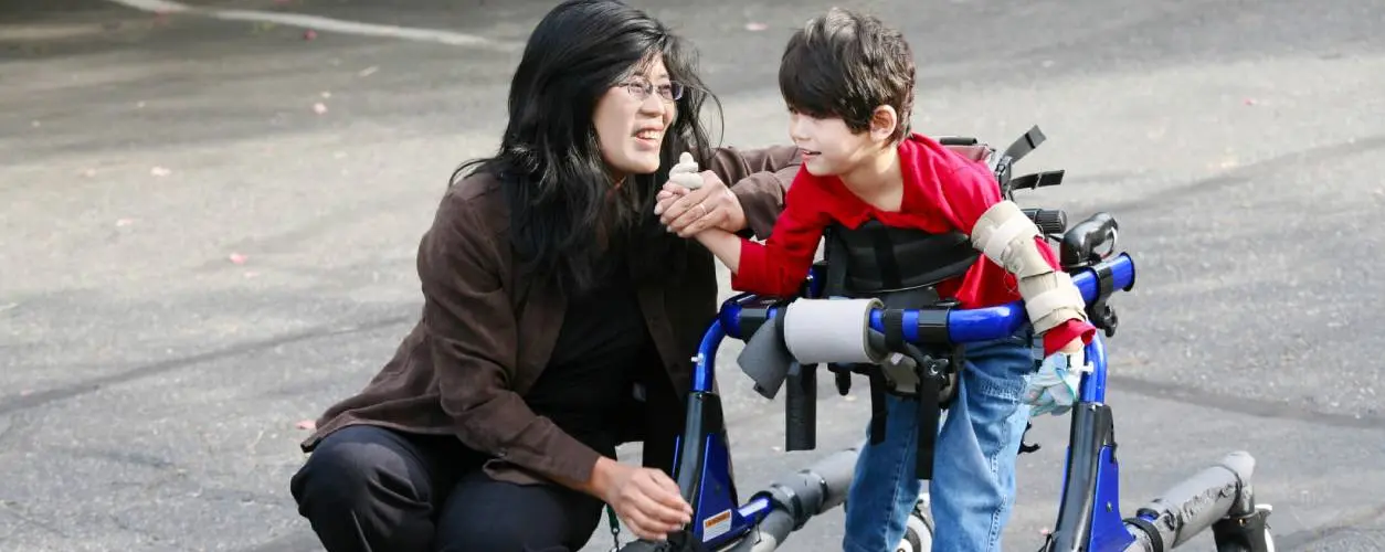 A caregiver assisting a child with cerebral palsy using a walker