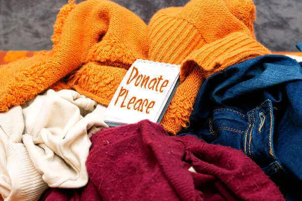 Pile of donations for a warm winter clothing drive. Small note book reads: "Donate please".