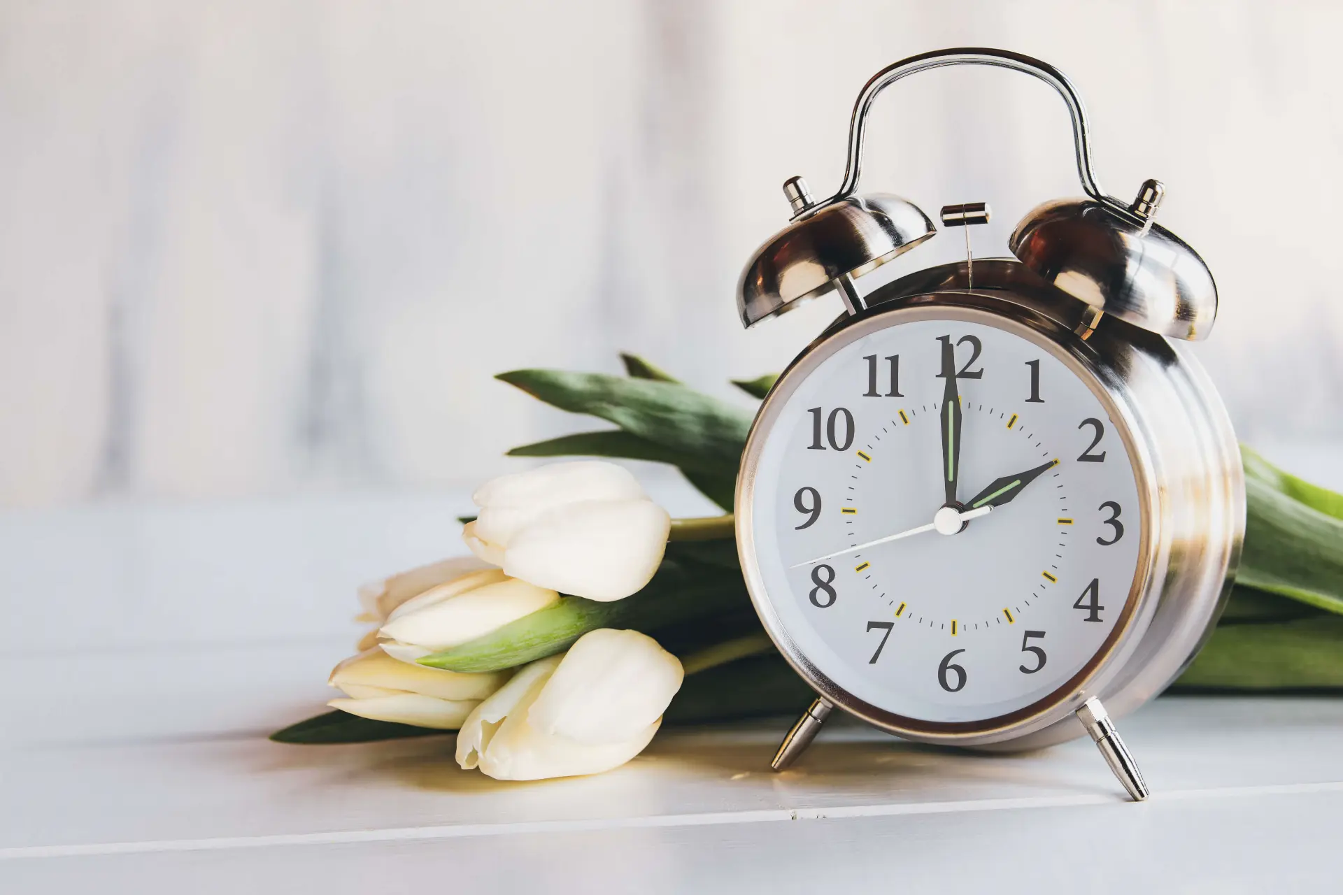 a clock that has just been set one hour ahead for daylight saving time sits in front of white tulips