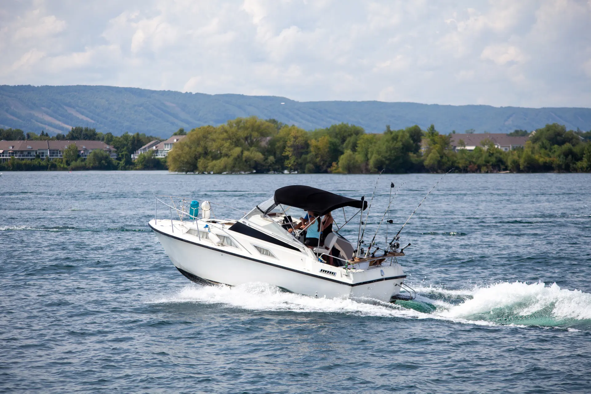a small white boat sets out on a lake on a partly clear day
