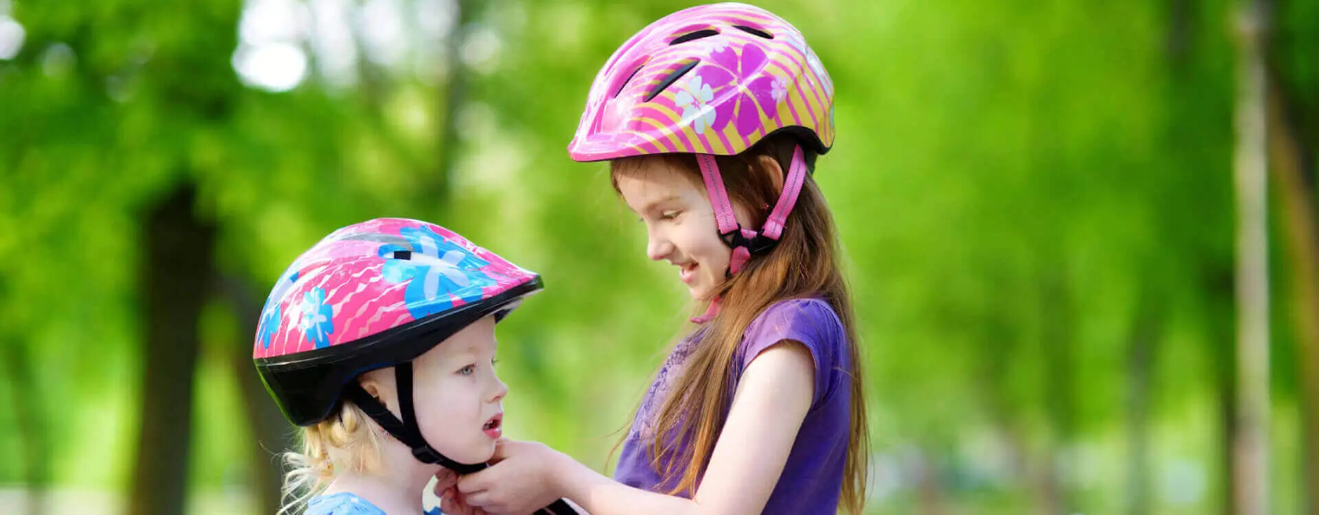Big sister helping her little sister to put a bicycle helmet on