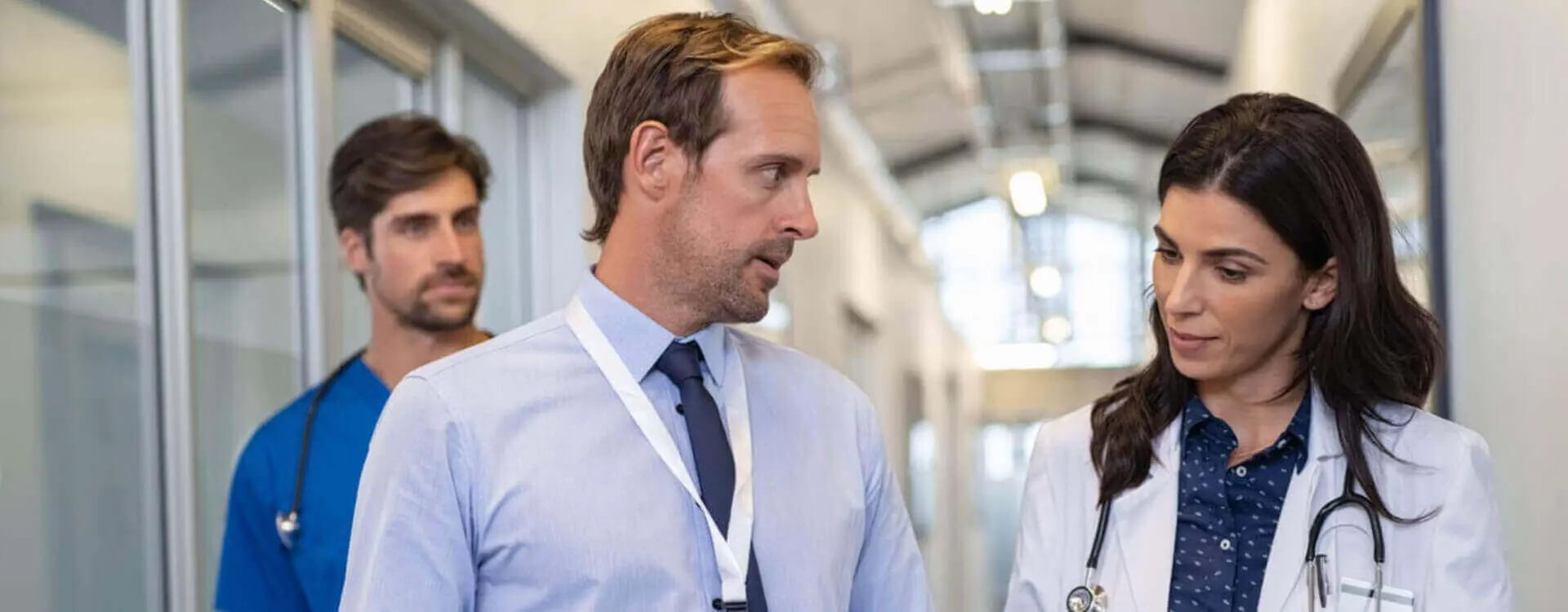 a female doctor having a discussion with a male walking in a hospital hallway with a male nurse behind them.