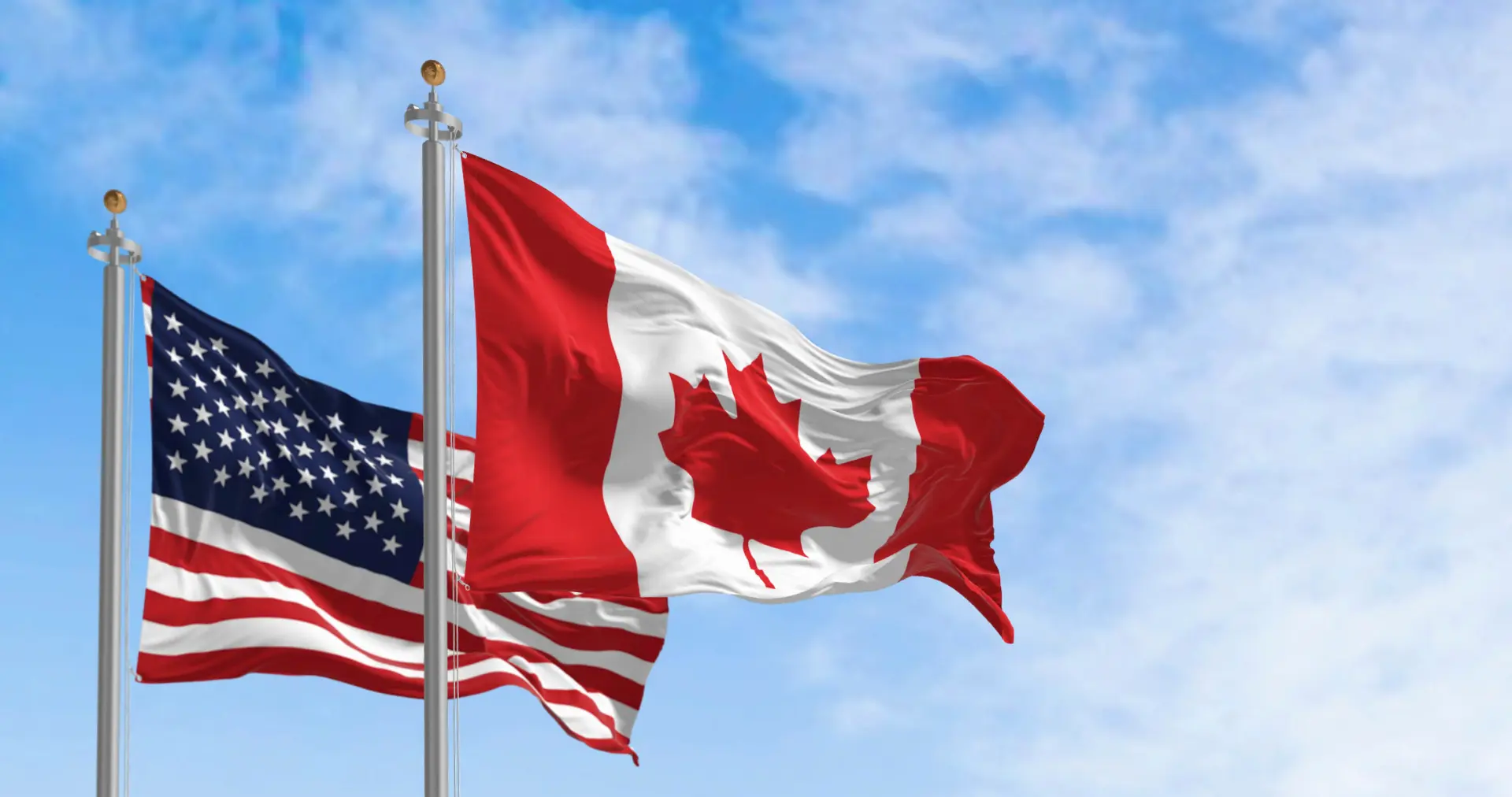 Canadian and American flags wave in the wind at a land border crossing between the two countries