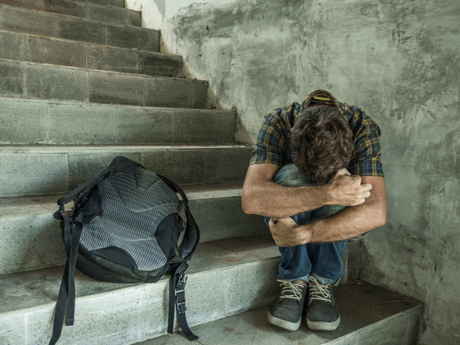 Depressed student sits on staircase hugging knees.