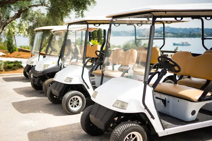 four golf carts lined up in a row at a golf course on a lakefront