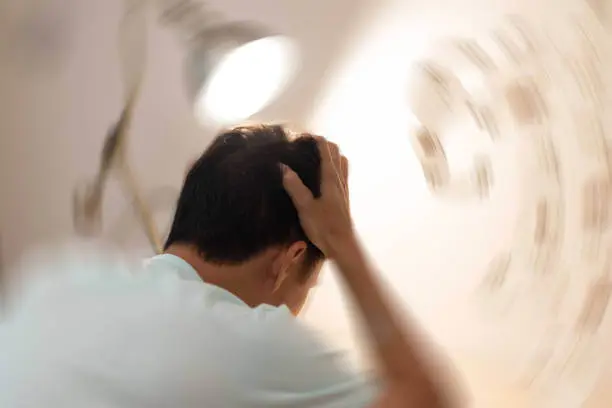 Man sitting with his back to the camera, his hands are on his head. The room is spinning in the background.