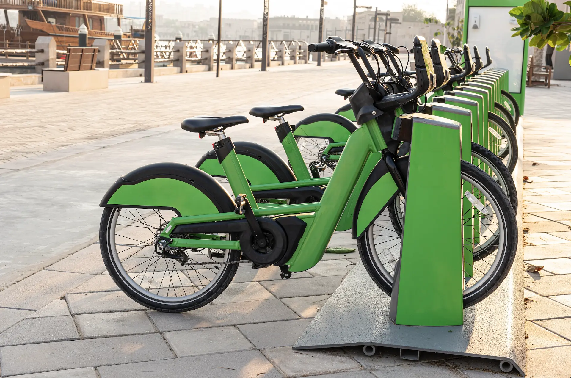 green e-bikes are locked at a docking station on a pier