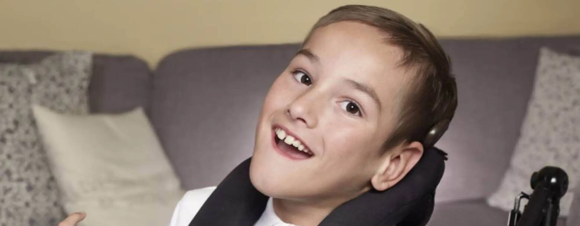 Disabled young boy in wheelchair smiling and happily looking at camera in his living room