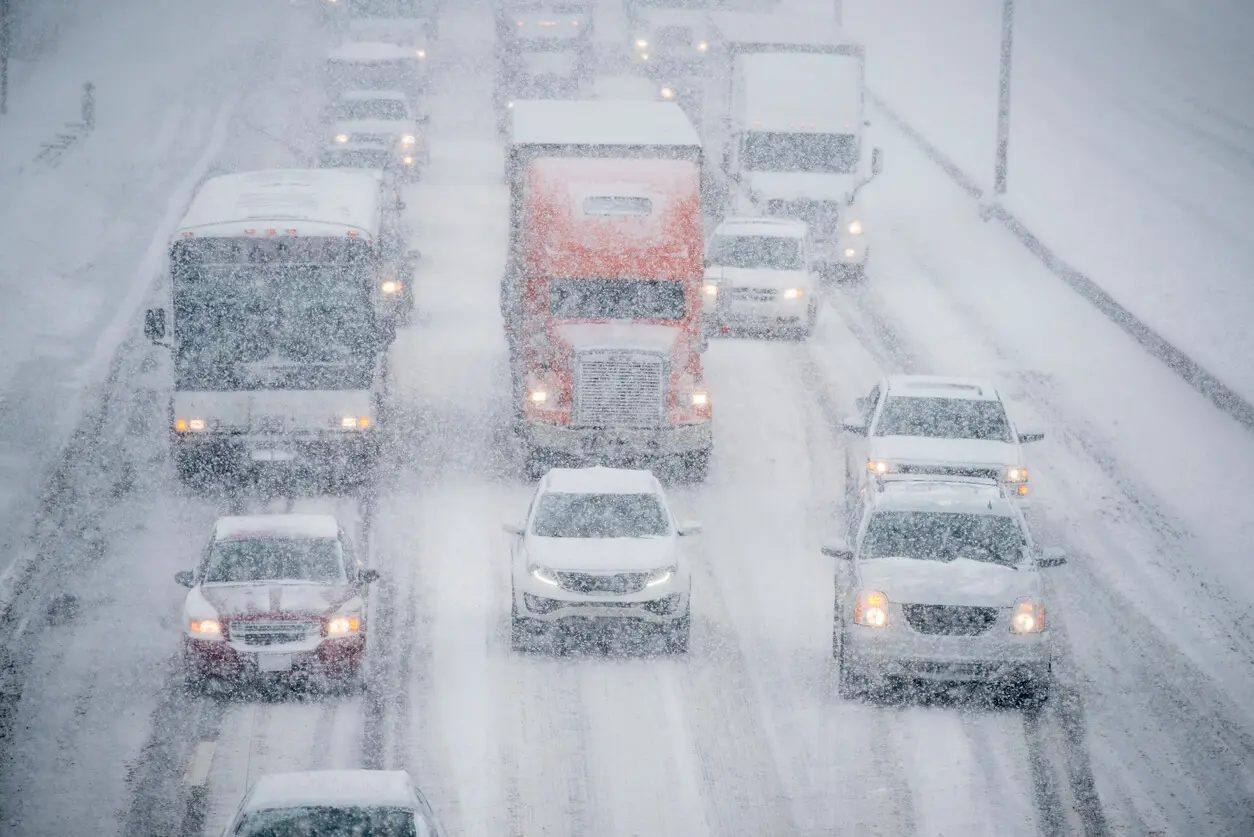 Several vehicles are traveling slowly down a multi lane road on an icy stormy day