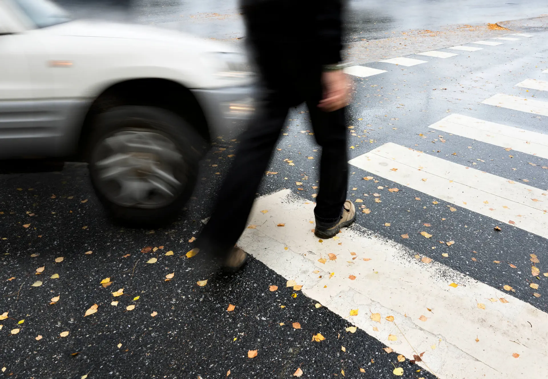 pedestrian about to get hit by a car at a crosswalk on slippery wet pavement