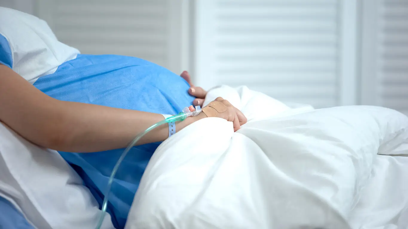 Pregnant woman in hospital bed with IV, risk of placental abruption