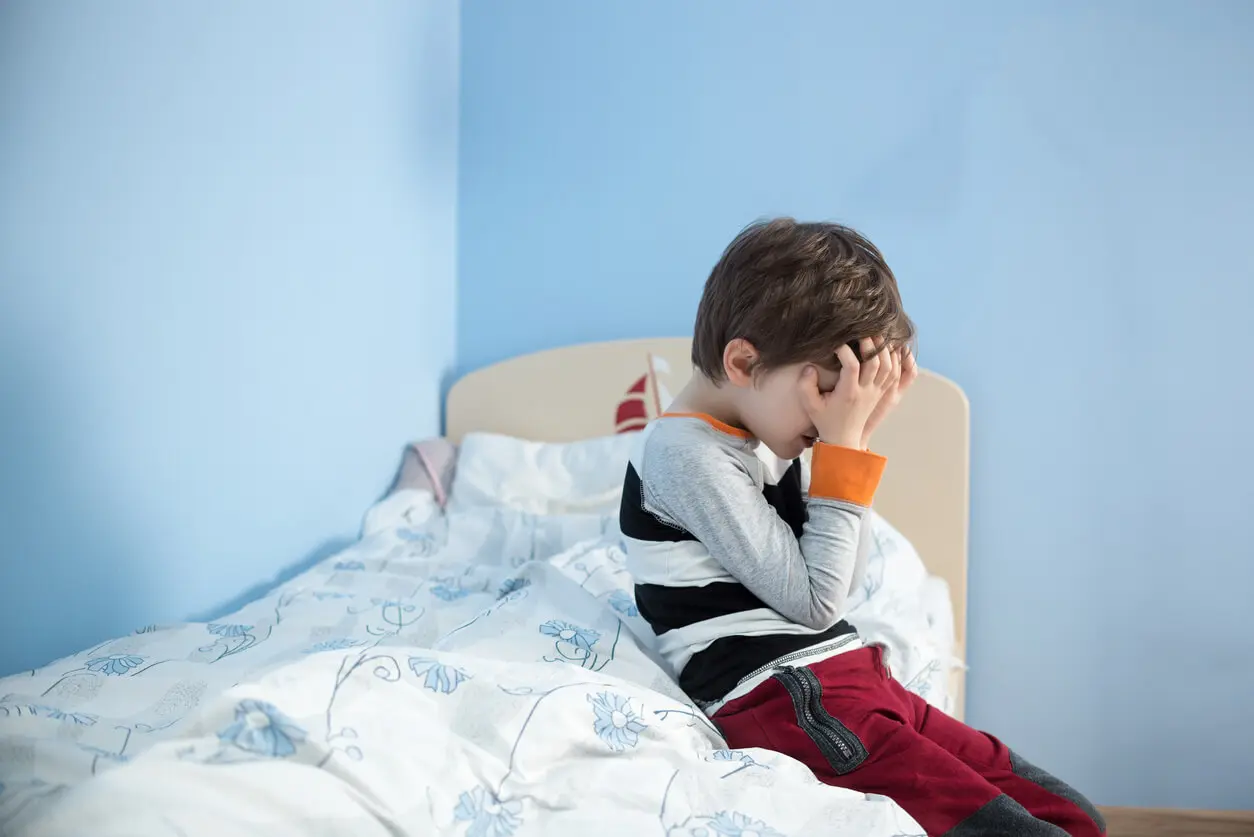 sad-young-boy-sitting-on-edge-of-bed-covering-face