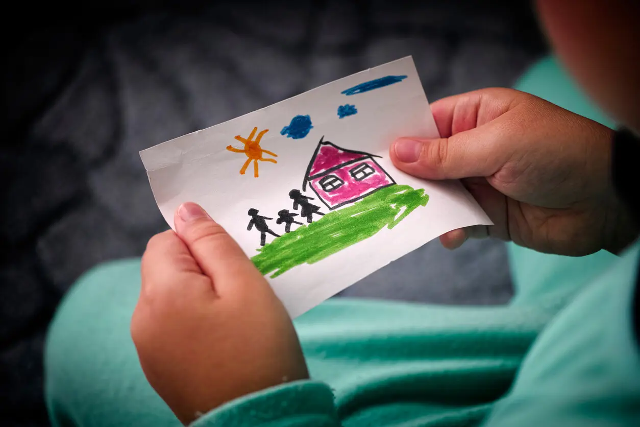 Child holds hand-drawn picture of house and family.