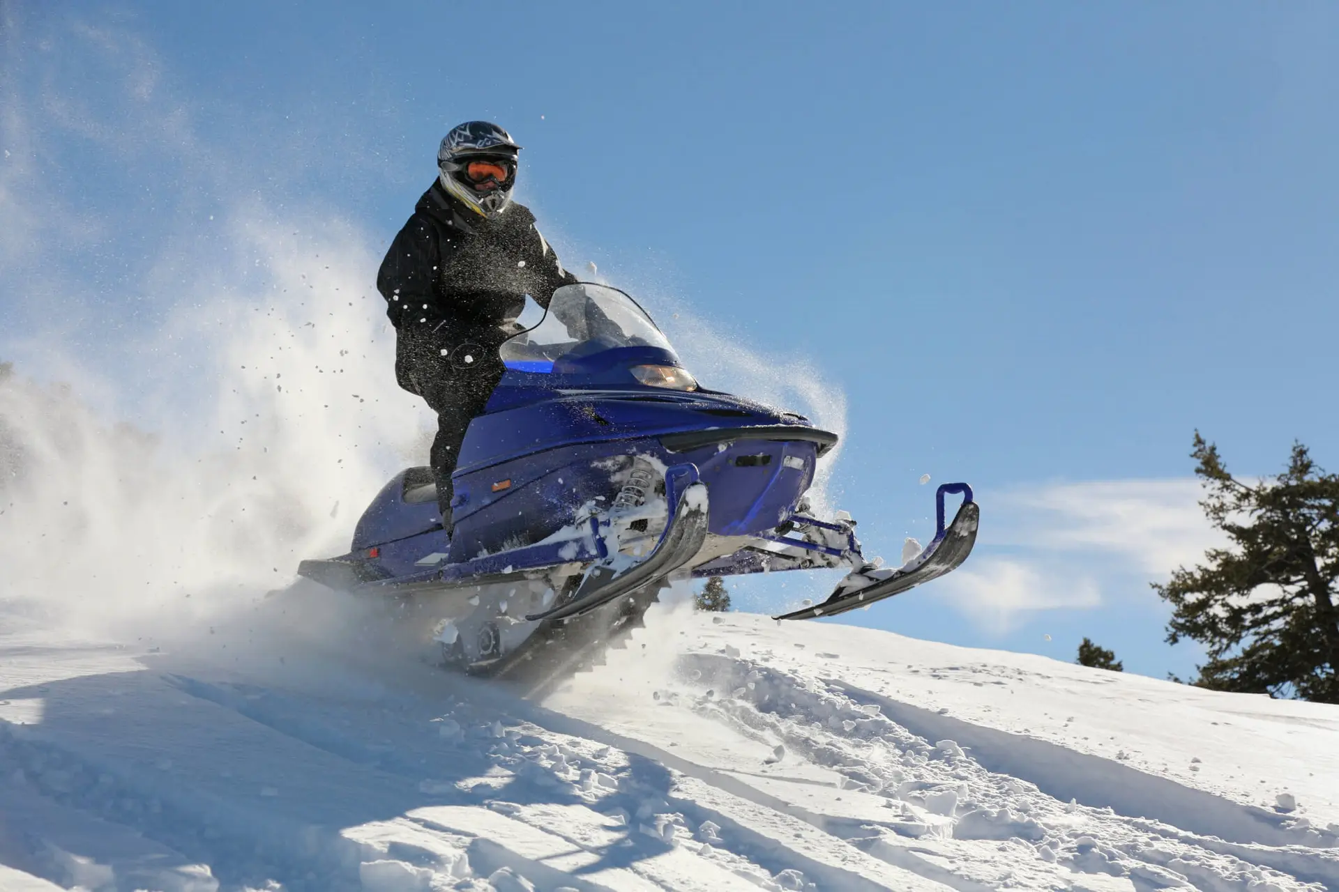 a boy rides a blue snowmobile during the winter on a snowy path on a sunny day