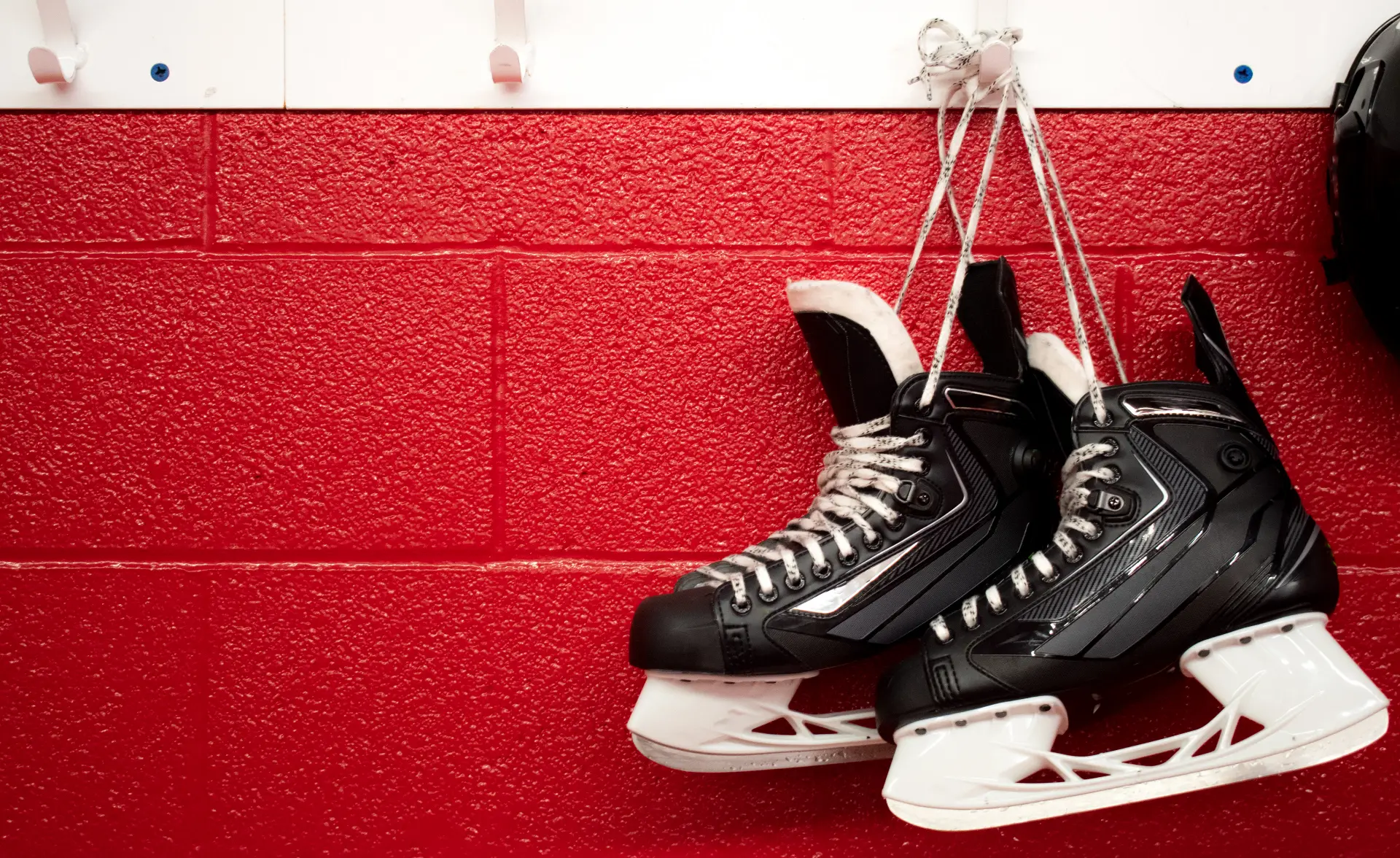 a pair of ice hockey skates hangs on a hook at an ice rink against a bright red brick wall