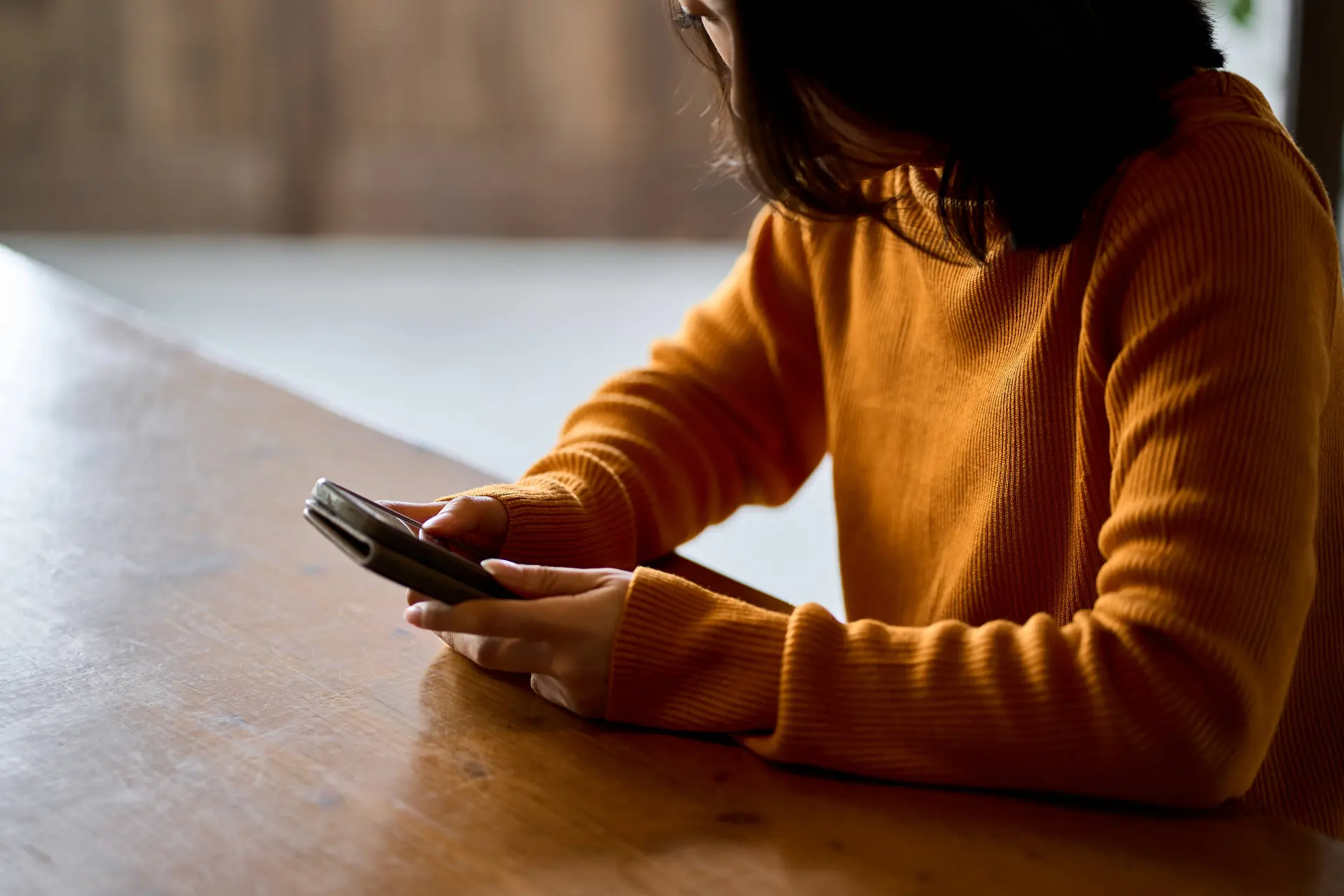 a person in an orange sweater is potentially reading about a BC court ruling on sexual assault defamation and its impact on survivors on their phone