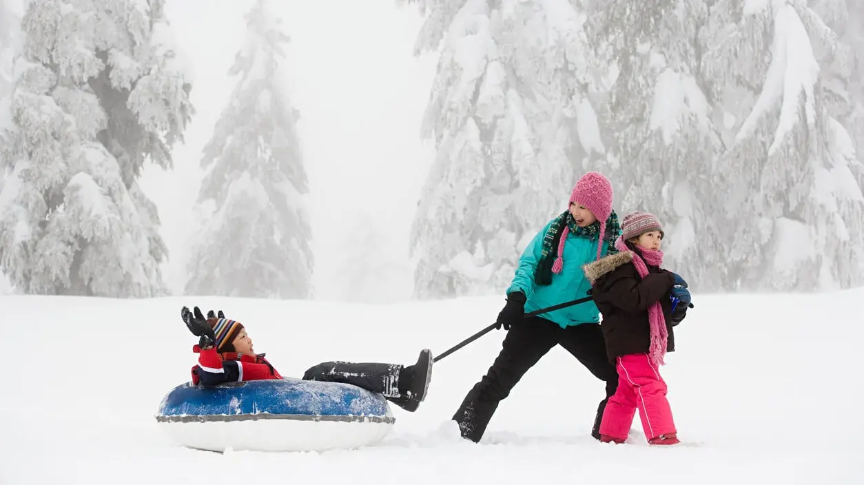 two children pull a third child in a tube when partaking in winter activities on a snowy day