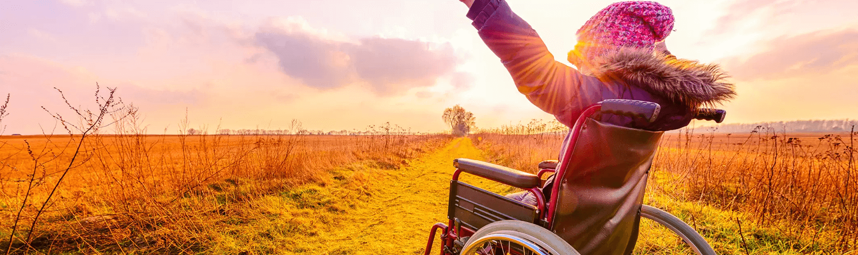 Child in wheelchair with arms up in a field