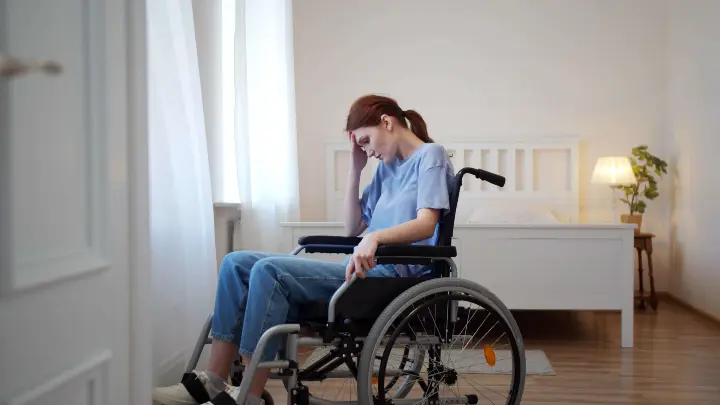 A woman in a wheelchair is upset and has her head in her hands