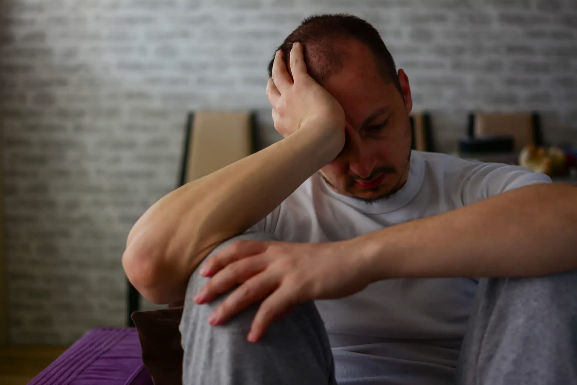 Sad unhappy man sitting on the sofa and holding his forehead while having headache. Unpleasant pain and discomfort.