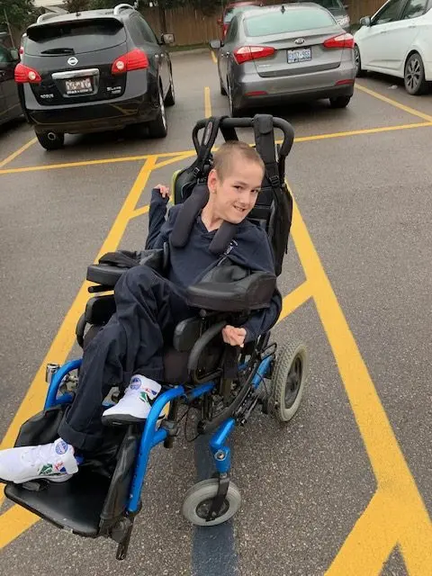 young boy in a wheelchair in a parking lot