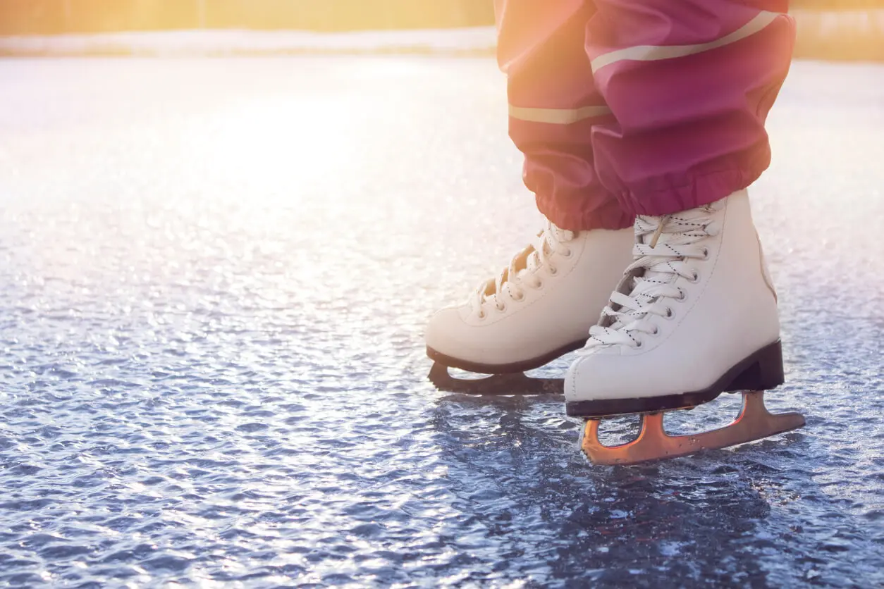 Close-up view of a young girl wearing white figure skates, skating on a frozen lake on a cold sunny winter day.