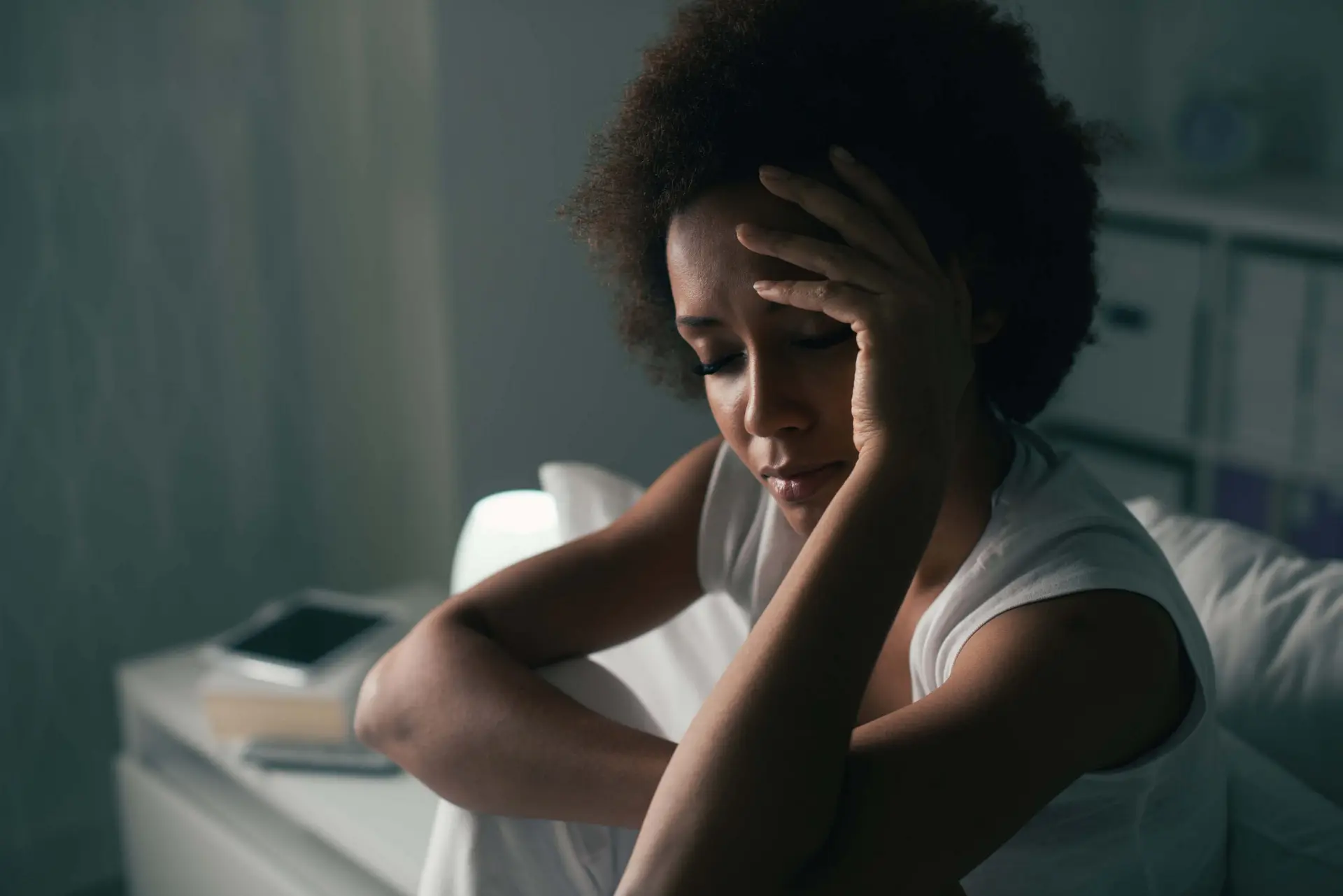 Sad depressed woman sitting in bed and touching her forehead